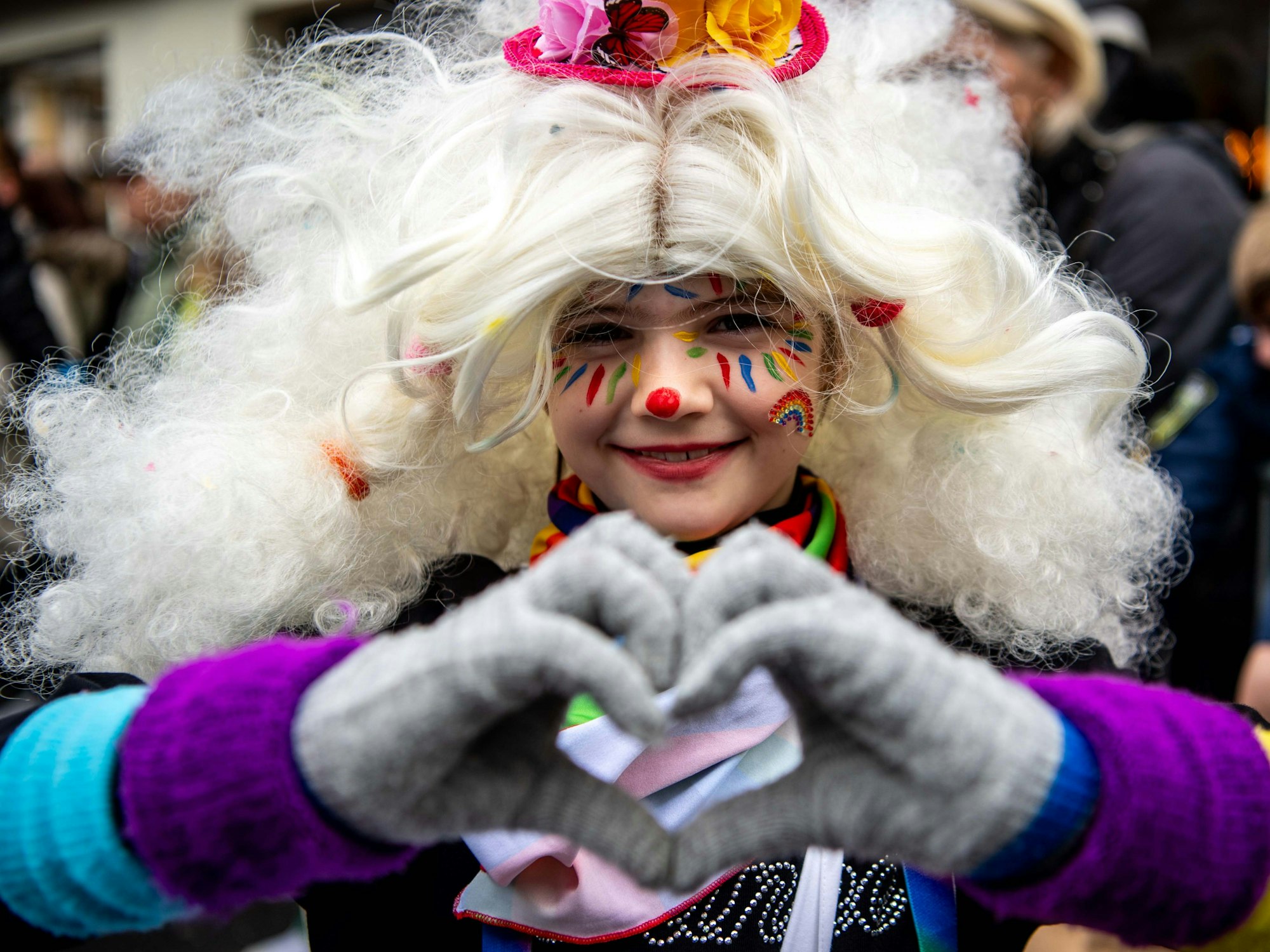 Das Bild zeigt ein Mädchen, das als Clown verkleidet ist und mit den Fingern ein Herz geformt hat.