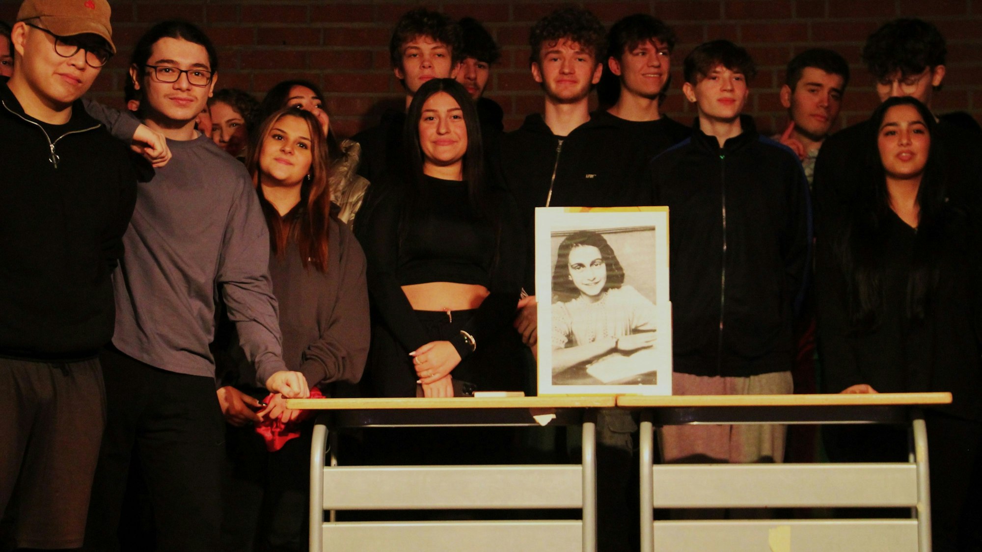 Viele Schüler stehen hinter einem Bild von Anne Frank.