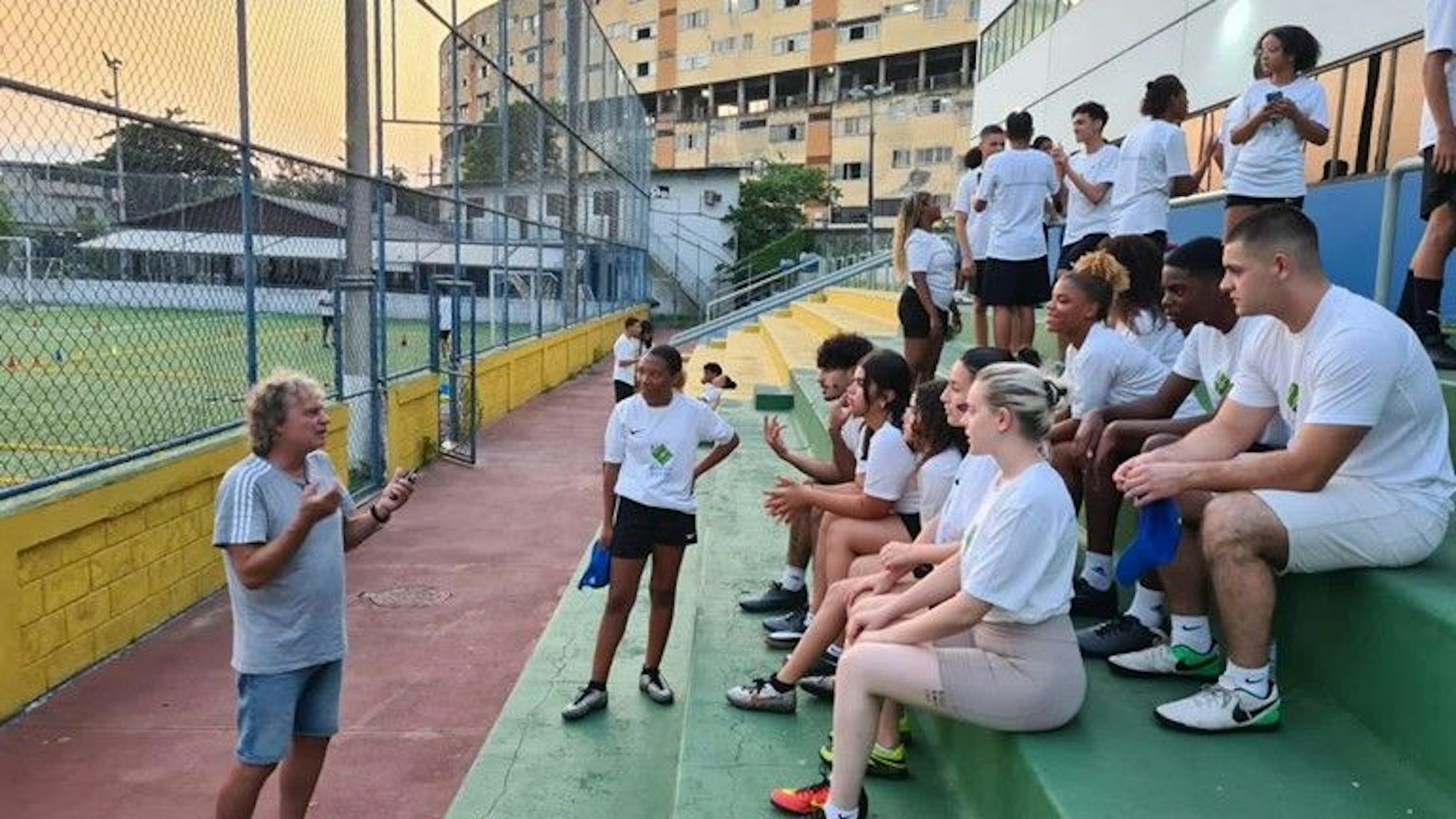 Ein Mann mit blonden Locken spricht zu Schülern, die auf den Stufen eines Stadions in Rio sitzen.