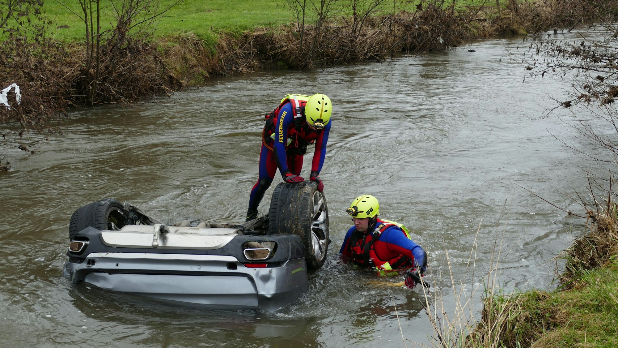 Zwei Feuerwehrleute in Spezialanzüge durchsuchen den zu großen Teilen unter Wasser liegenden BMW X 5.