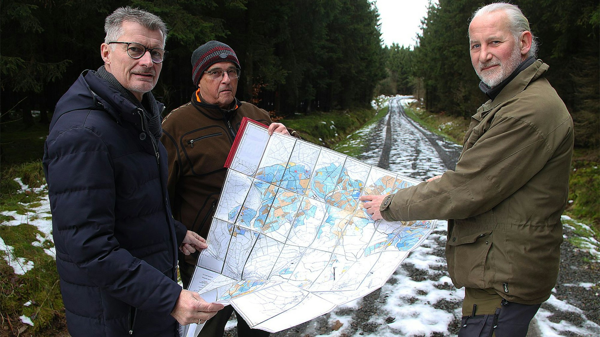 Drei Männer stehen auf einem leicht verschneiten Waldweg und halten eine Karte in der Hand.