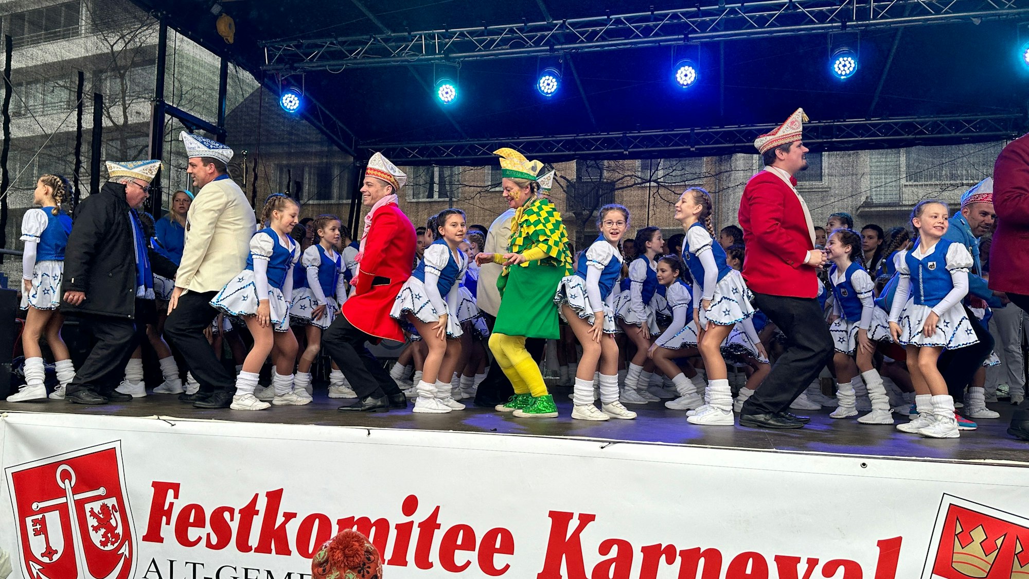 Auf einer Bühne tanzen Männer und blau-weiß-kostümierte Mädchen.