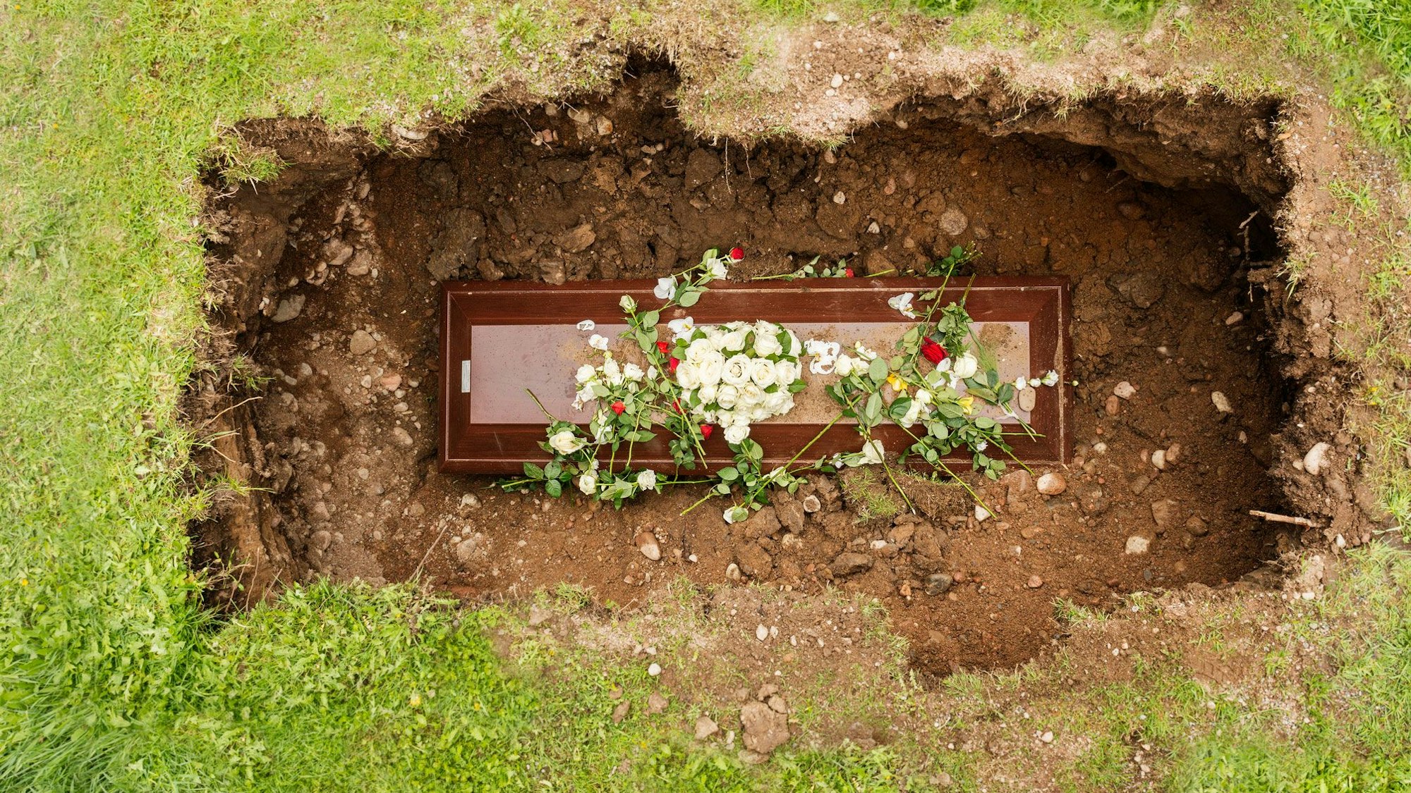 Ein Sarg mit Blumen in einem geöffneten Grab