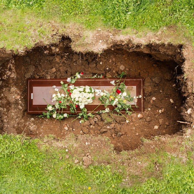 Ein Sarg mit Blumen in einem geöffneten Grab