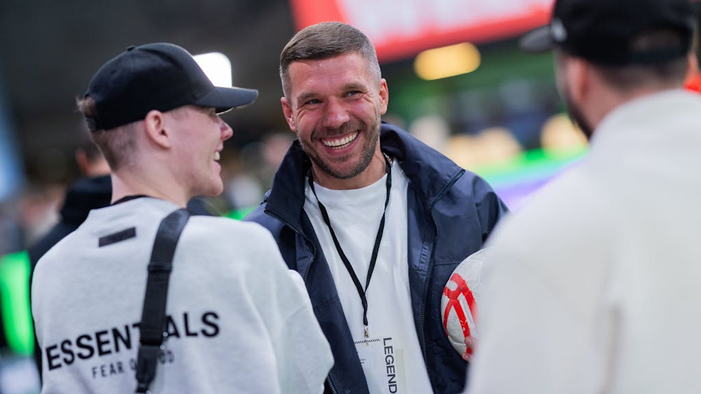 Lukas Podolski mit breitem Lachen bei einem Gespräch.