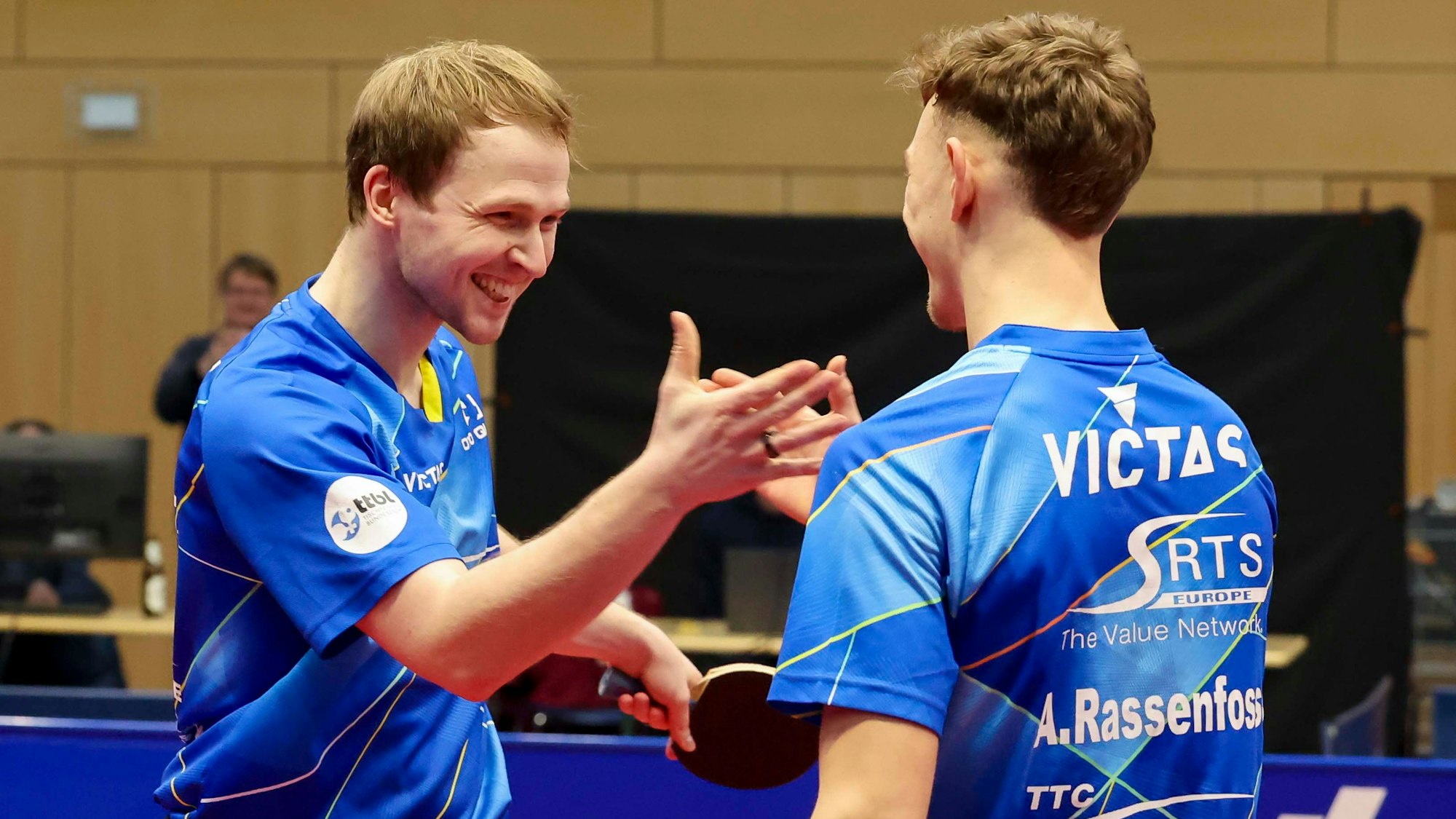 Die beiden Tischtennisspieler Benedikt Duda und Adrien Rassenfosse lachen und schlagen mit den Händen ein.