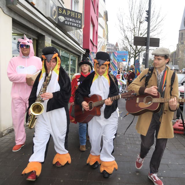 Mit Gitarren und Saxofon zieht eine Gruppe eine Straße entlang.