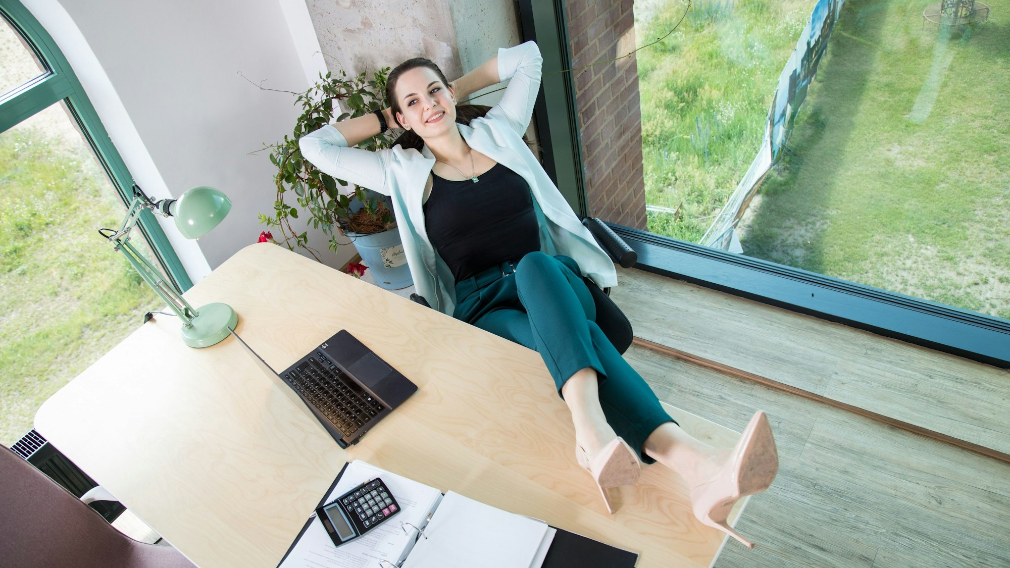 Eine Frau legt die Beine auf den Bürotisch und sieht entspannt aus.