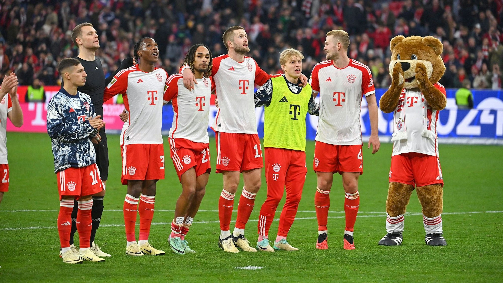 Die Bayern-Profis Bryan Zaragoza, Manuel Neuer, Mathys Tel, Sacha Boey, Eric Dier, Frans Krätzig und Eric Dier feiern gemeinsam mit Maskottchen Berni vor den Fans.