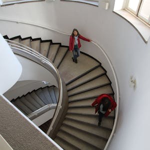 Zwei Frauen lauen eine gewundene Treppe herunter.&nbsp;