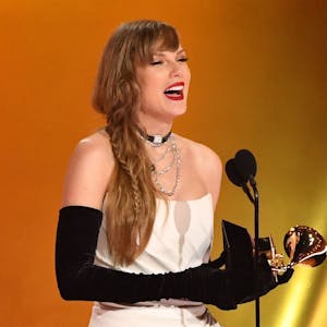 Taylor Swift hält einen Grammy-Preis in der Hand. Sie trägt ein weißes schulterloses Kleid und lange schwarze Handschuhe.