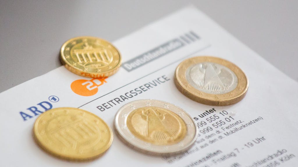 Euromünzen liegen auf einem Anschreiben zur Anmeldung für die Rundfunkgebühren, neben den Logo von ARD (l-r), ZDF und Deutschlandfunk.