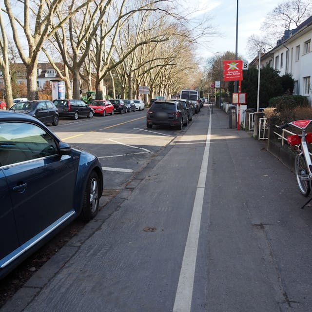 Blick in eine Straße mit parkenden Autos und einem für Radfahrer und Fußgänger aufgeteilten Gehweg.