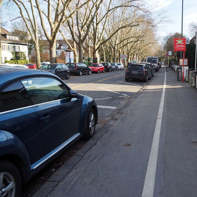 Blick in eine Straße mit parkenden Autos und einem für Radfahrer und Fußgänger aufgeteilten Gehweg.