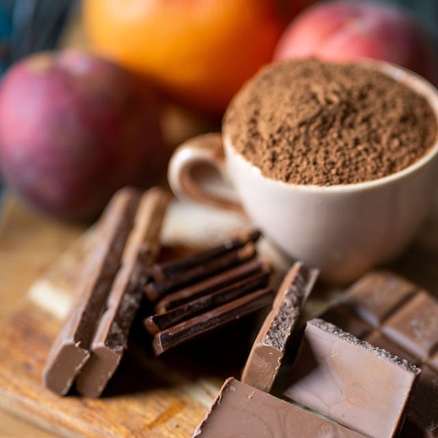 Vollmilchschokolade liegt neben einer mit Kakaopulver gefüllten Tasse auf einem Holzbrett in der Küche.