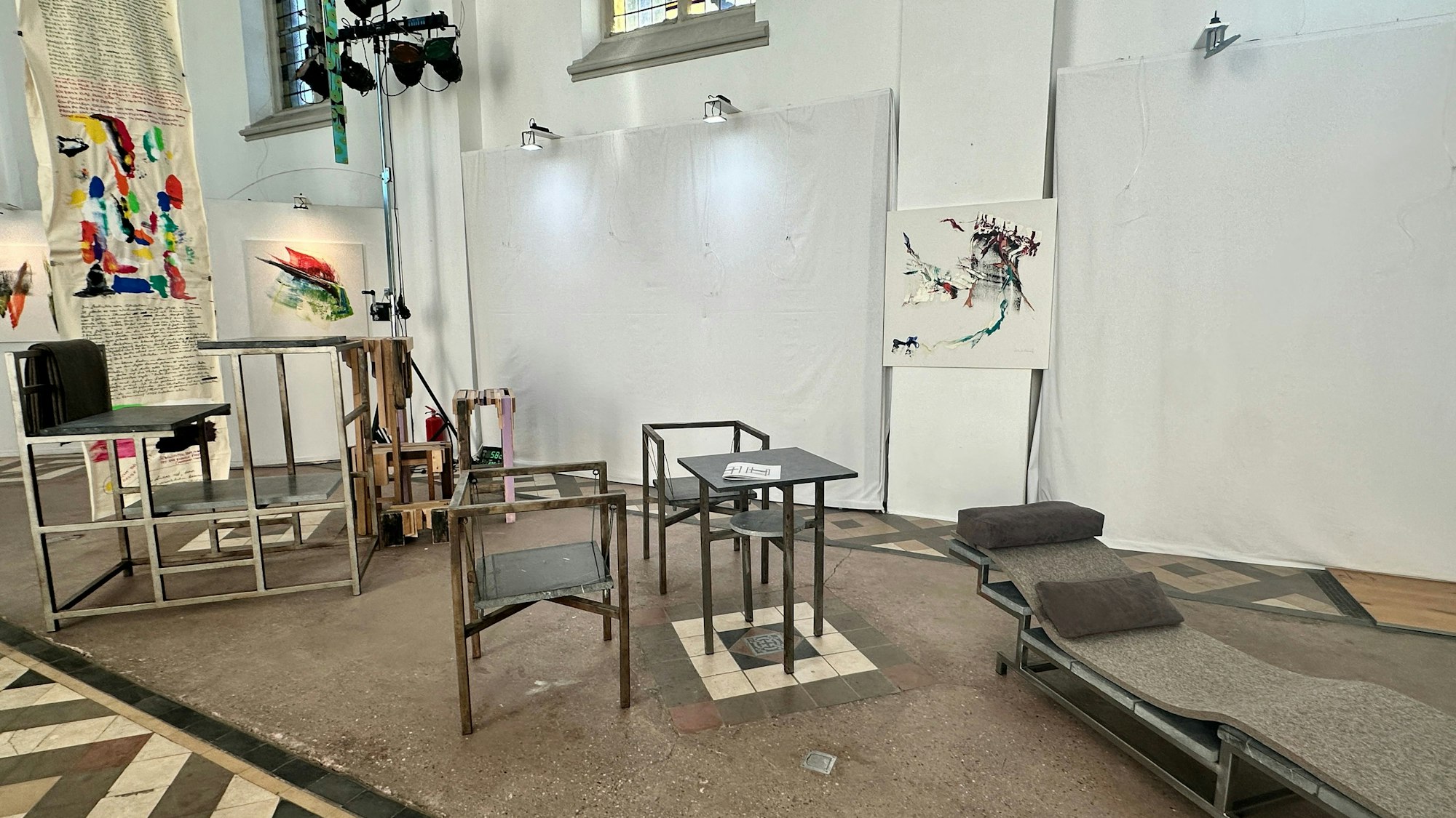 Stühle, eine Liege und Bilder sind in einem Kirchenraum ausgestellt.