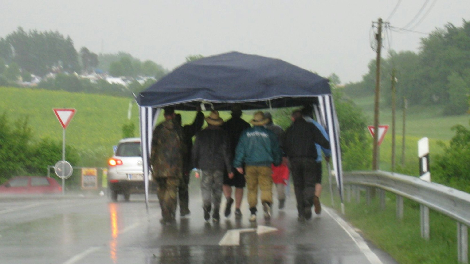 Man sieht eine Männergruppe unter einen Pavillon gedrängt, die durch den Regen läuft.