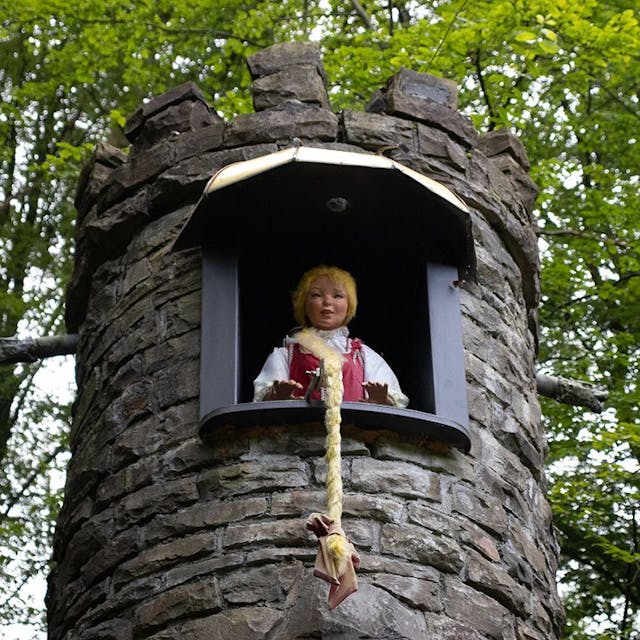 Eine Puppe, die Rapunzel darstellt, schaut aus einem Turm, der das Märchenhaus im Märchenwald in Altenberg darstellt.