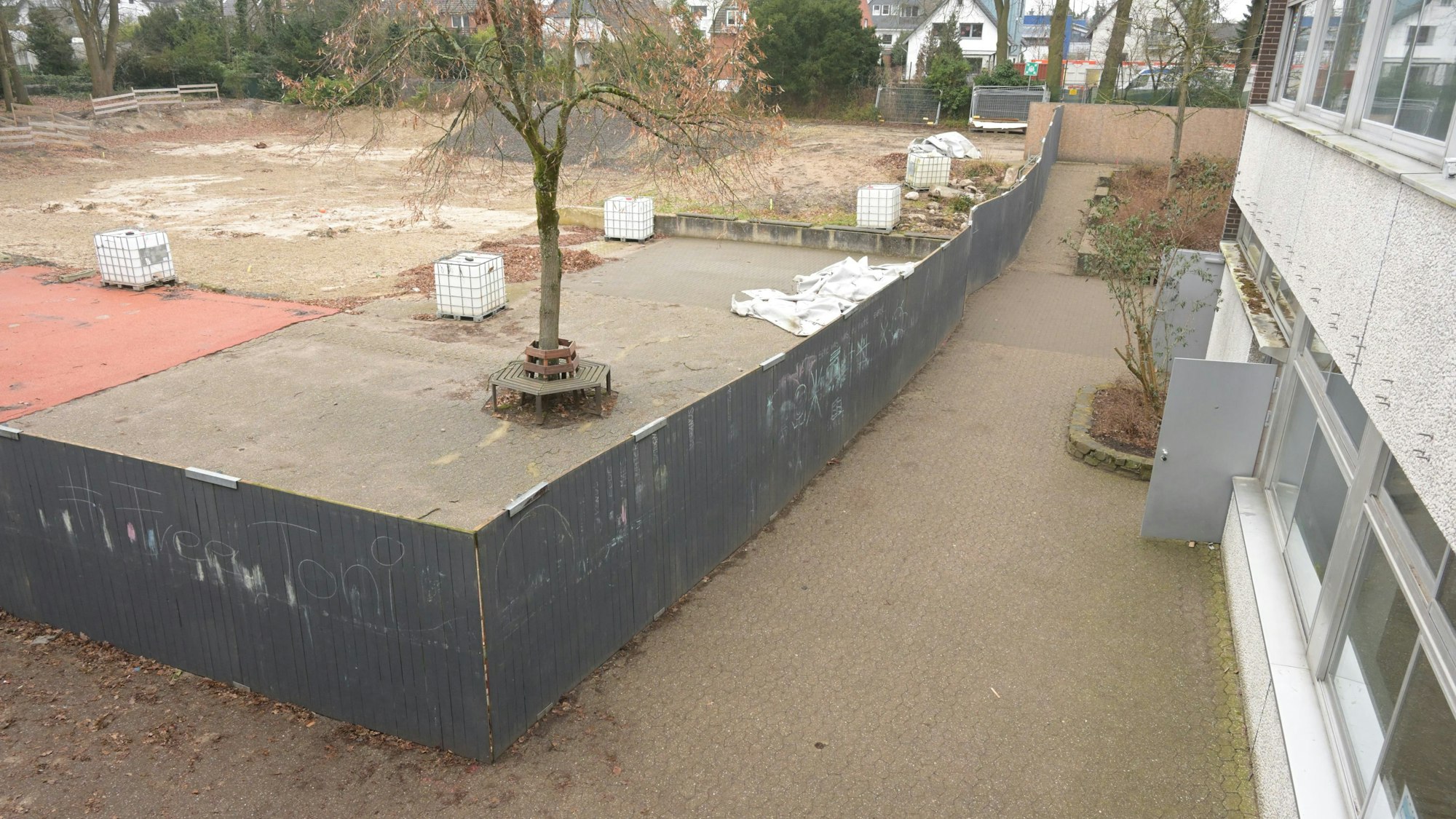 Links im Bild sieht man den schwarzen Bretterzaun, daneben liegt der schmale Schulhof-Gang, der an das Schulgebäude grenzt.