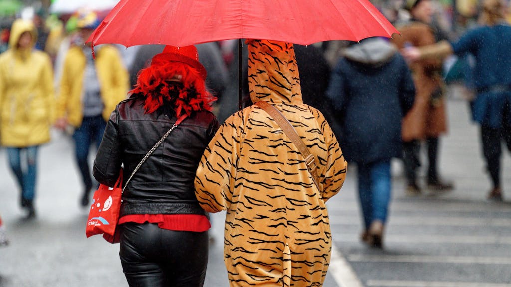 Verkleidete Karnevalisten unterwegs mit Regenschirm.