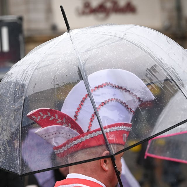 Ein Karnevalist mit Karnevalskappe steht unter einem Regenschirm. Es regnete zur Eröffnung der Karnevalssession dauerhaft.&nbsp;