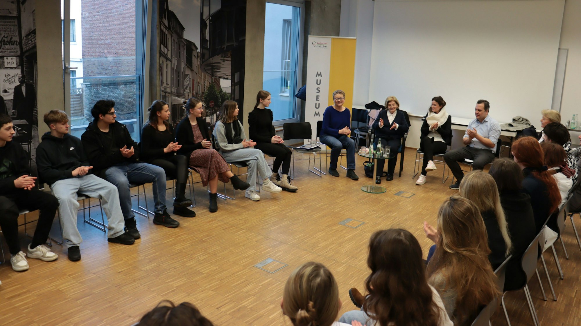 Eva Szepesi, Schülerinnen und Schüler und weitere Zuhörerinnen und Zuhörer sitzen im Museum in einem Kreis auf Stühlen.