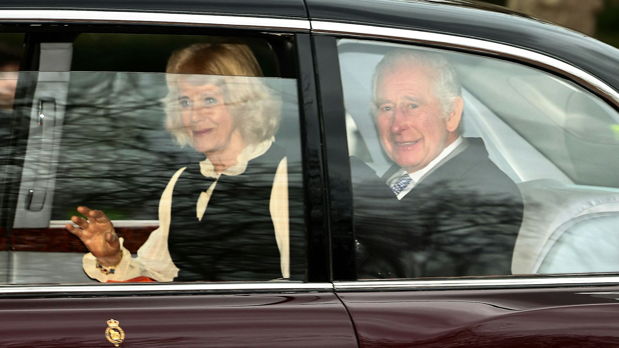 Königin Camilla und König Charles winken aus dem Auto.