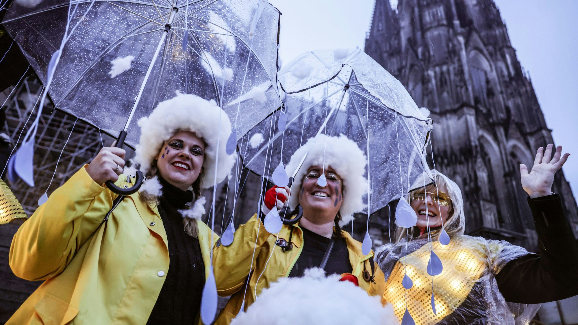 Karnevalistinnen stehen mit Regenschirmen am Dom.