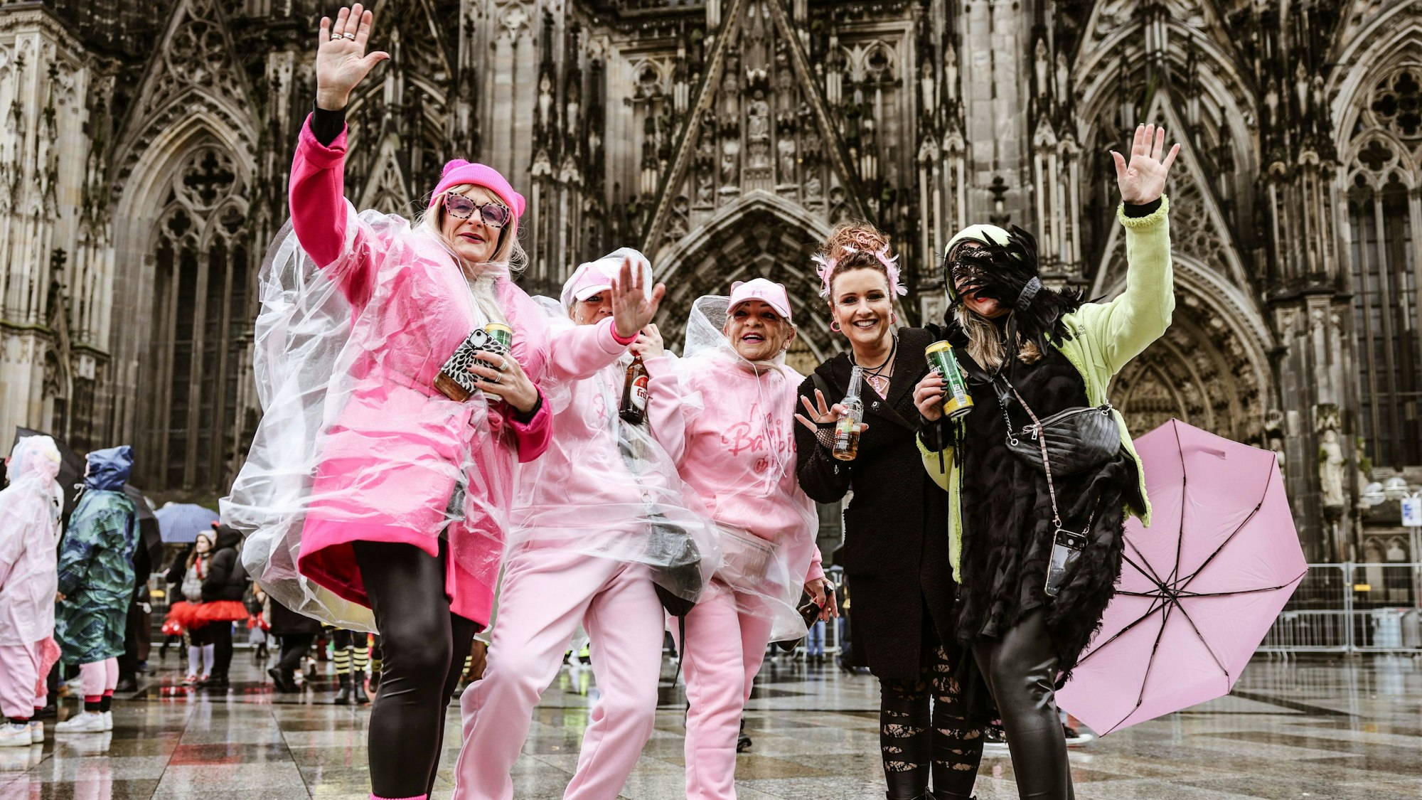 Karnevalistinnen feiern in Regenschutz vor dem Dom.