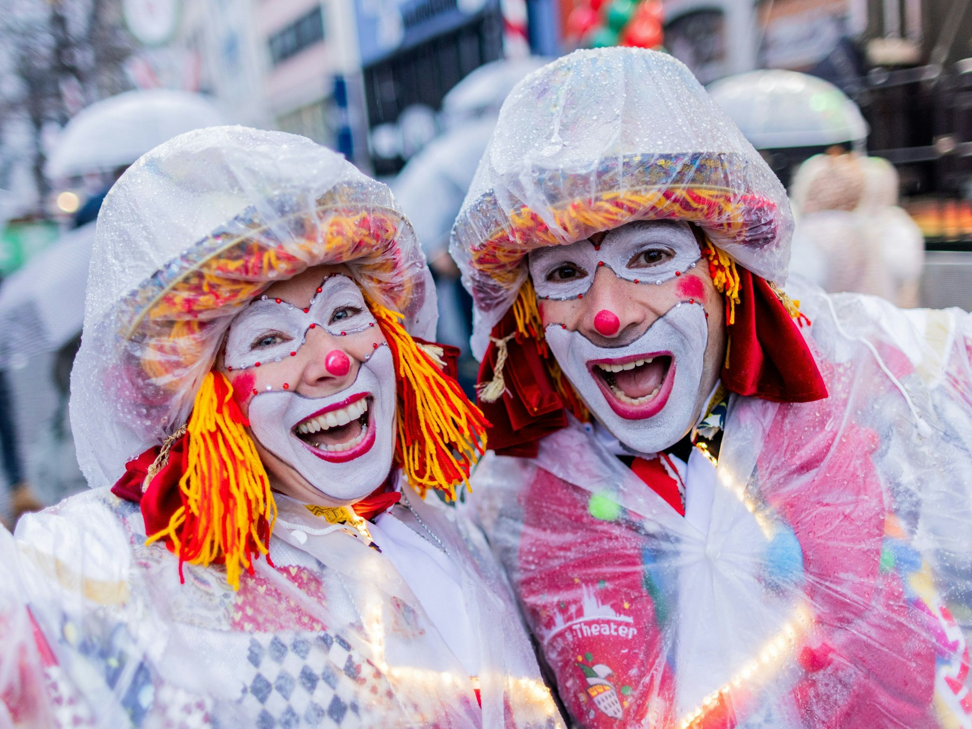 Zwei Clowns mit Regenschutz lachen in die Kamera.