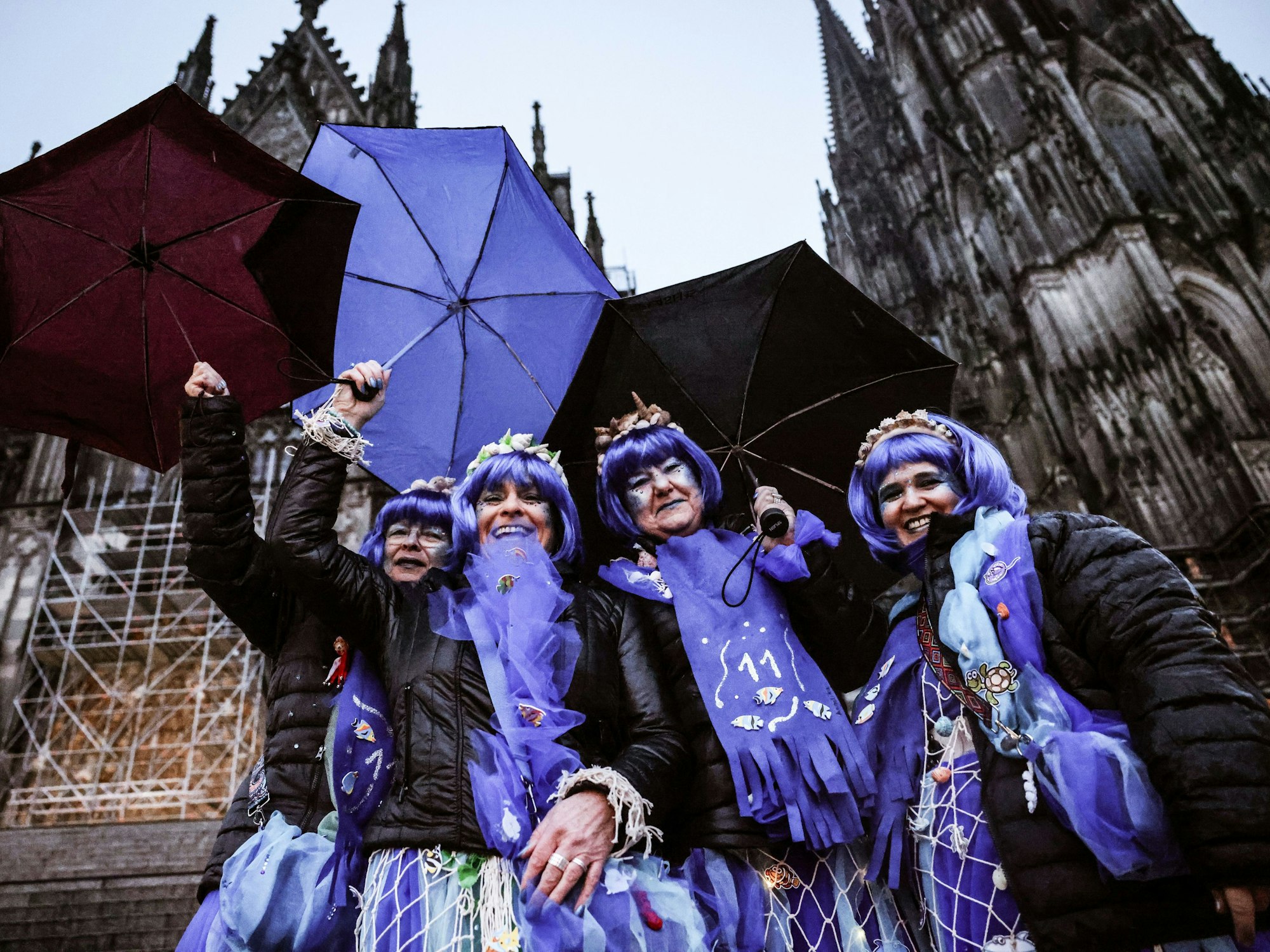 Karnevalistinnen stehen mit Regenschirmen am Dom.