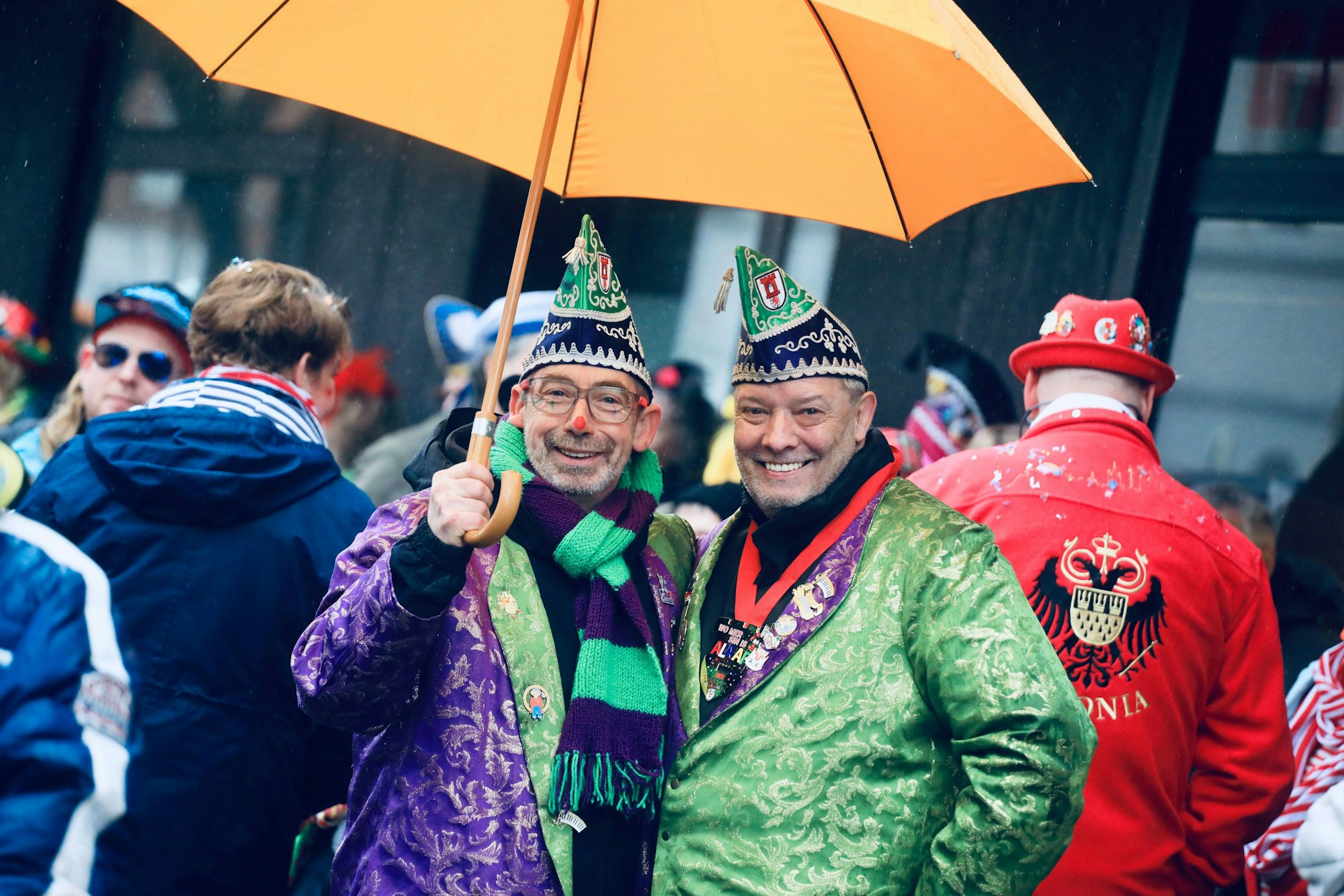 Zwei kostümierte Männer mit Schirm schauen in die Kamera.