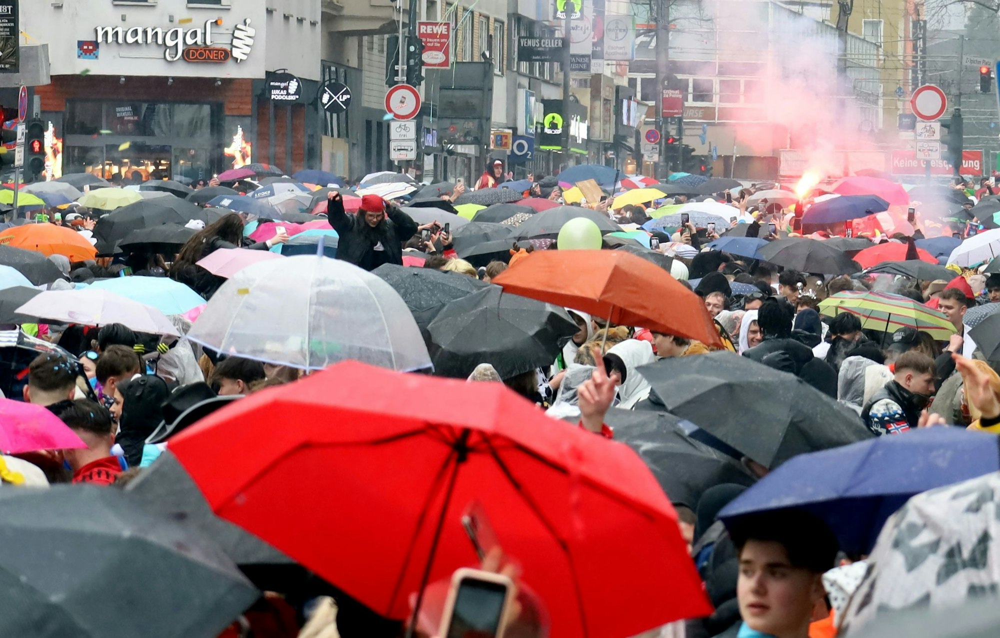 Blick auf Regenschirme auf der Straße, im Hintergrund zündet jemand ein Bengalo.