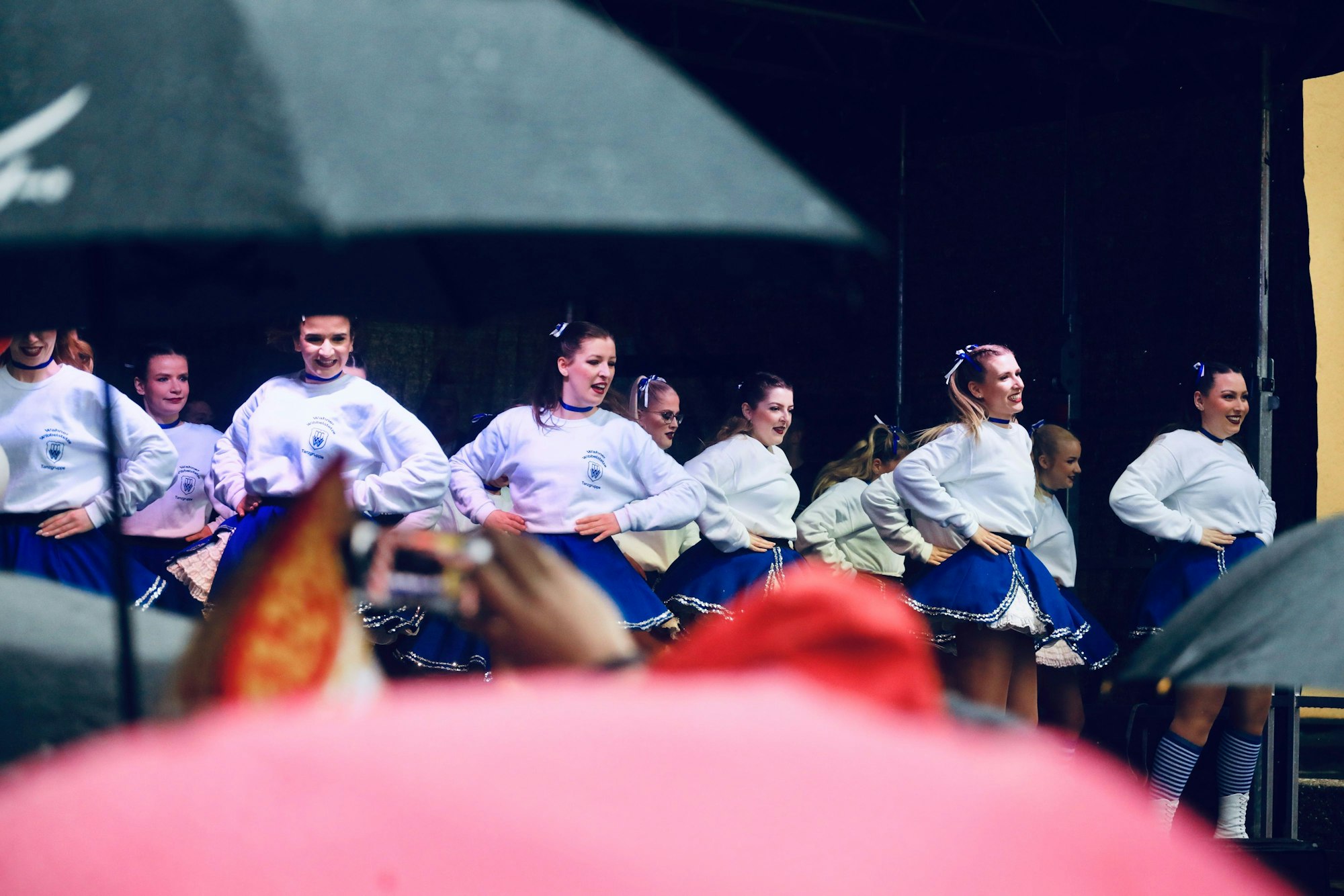 Blick durch Regenschirme hinweg auf eine Mädchen-Tanzgruppe, die auf der Bühne ihren Auftritt hat.