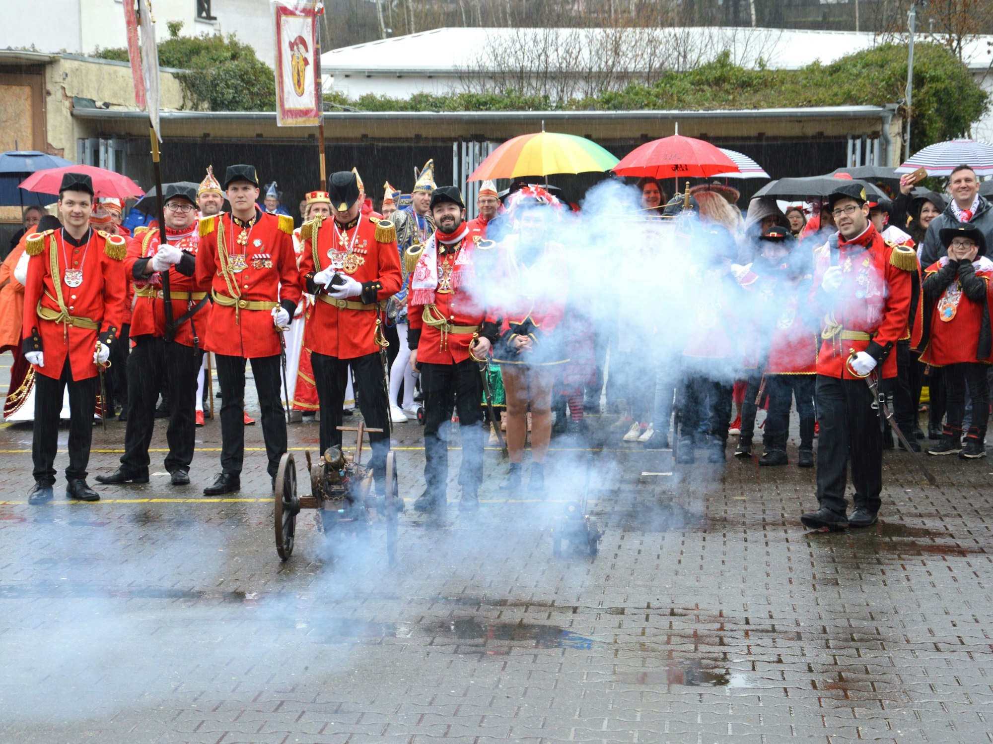 In rote Jacken und schwarze Hosen gekleidete Kaller Karnevalisten schießen mit einer Kanone beim Rathaussturm.