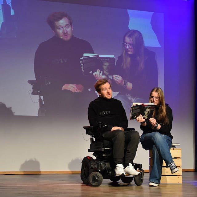 Samuel Koch (im Rollstuhl) auf der Bühne mit einer Schülerin, die ihm ein Buch hinhält.&nbsp;