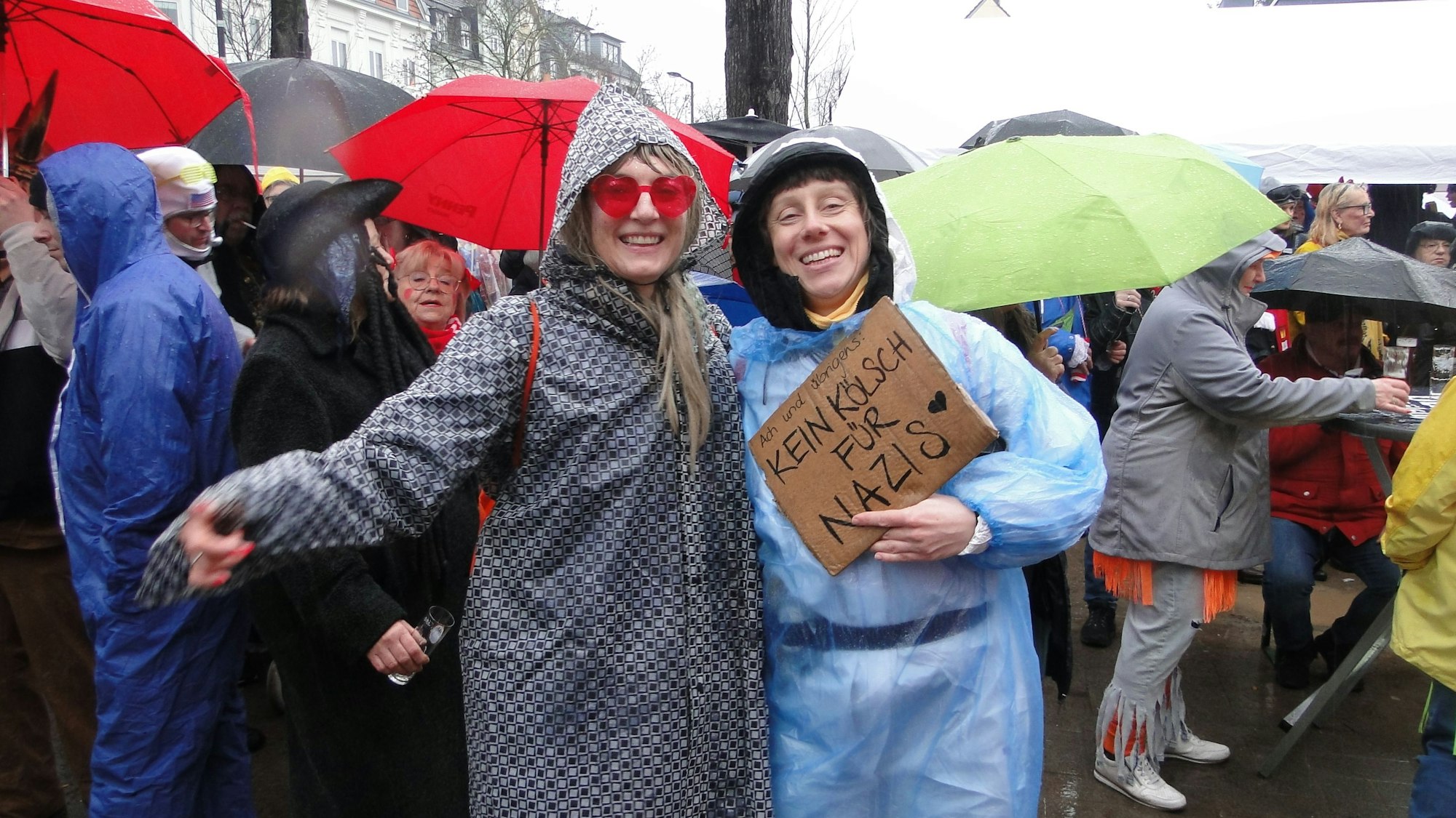 Menschen mit Regenschirmen stehen dicht beisammen, im Vordergrund zwei Frauen mit Regenjacken.