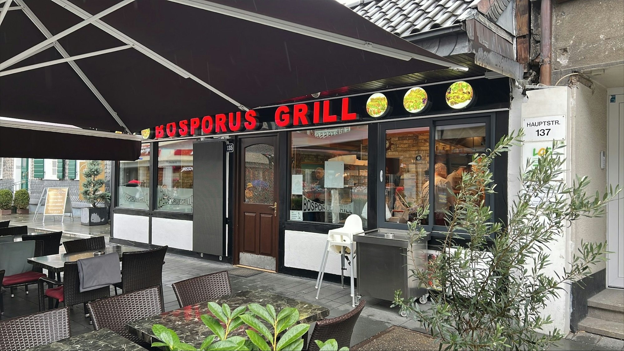 Das Restaurant Bosporus Grill in der Bergisch Gladbacher Innenstadt von außen. Ein Regenschirm ist über dem Außenbereich mit Stühlen gespannt.