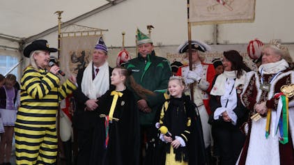 Auf dem Bild ist Frechens Bürgermeisterin und die beiden Prinzessinnen zu sehen. Hinter ihnen stehen viele karnevalistisch verkleidete Personen.