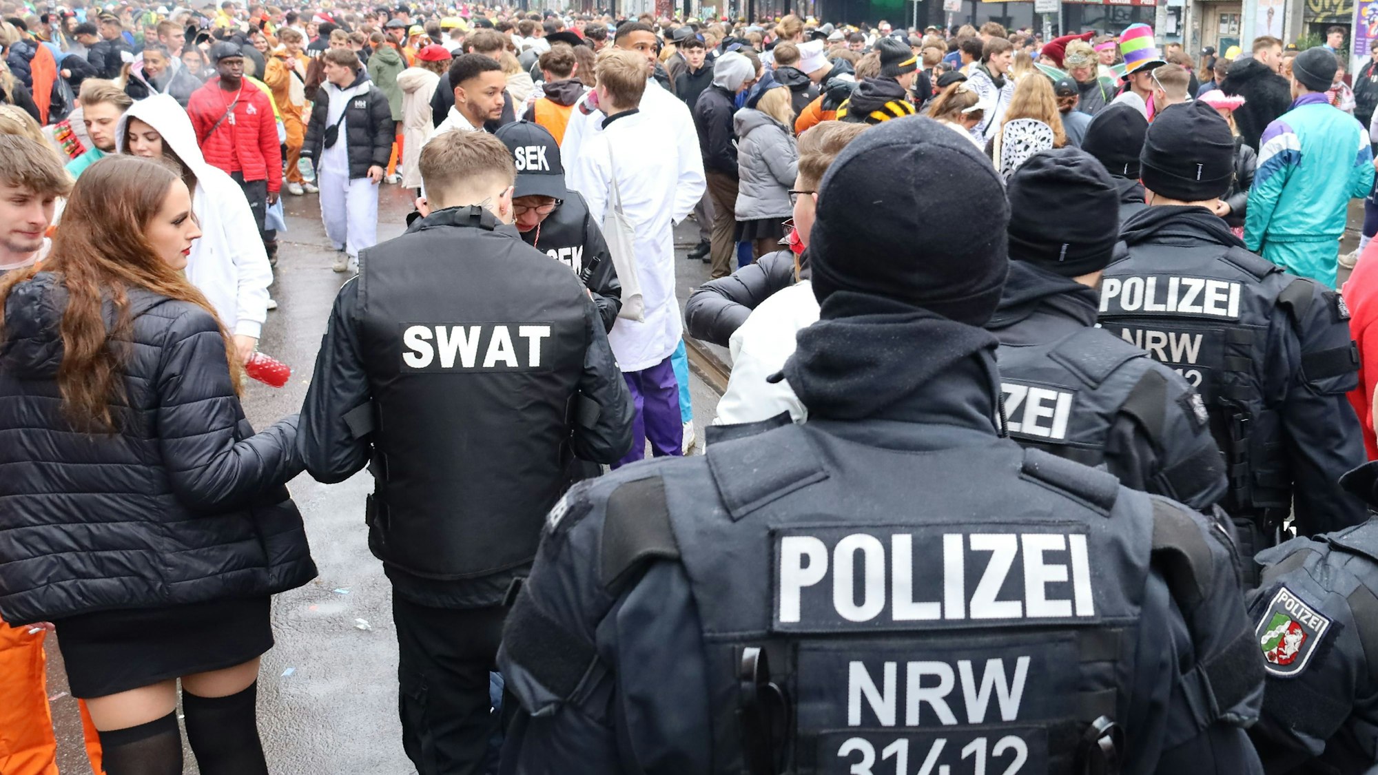 Wer ist hier der echte Polizist? Als „Swat“-Team verkleidete Jecke stehen hinter Polizeibeamten in Uniform.