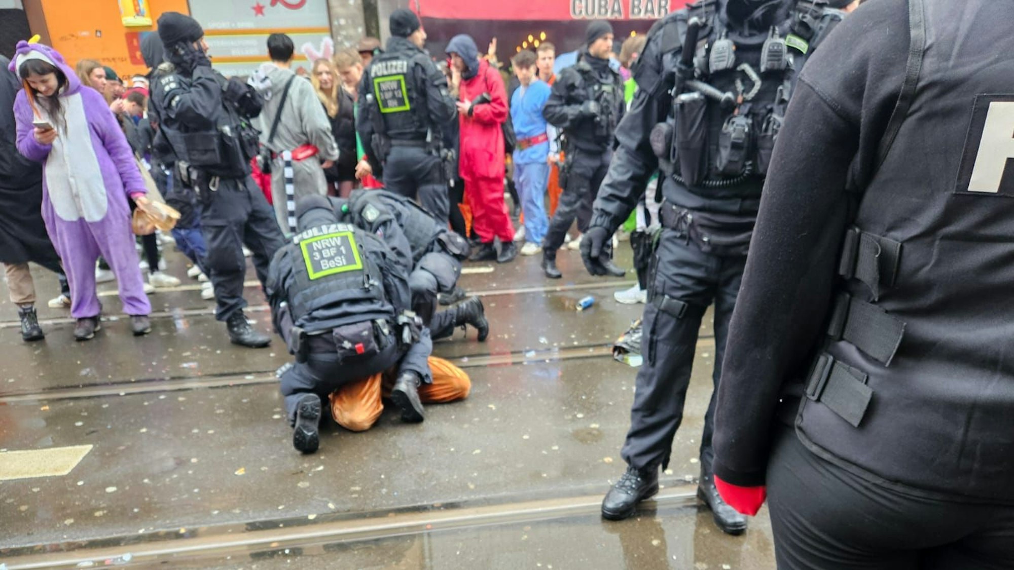 Zwei Polizisten fixieren im Getümmel der Zülpicher Straße einen Mann am Boden.