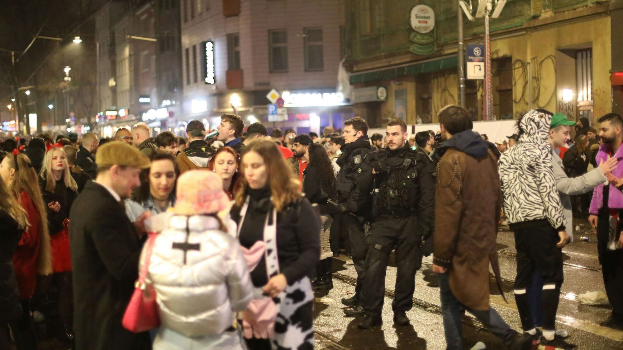 Karnevalisten stehen auf der Zülpicher Straße in der Nacht neben Polizisten.