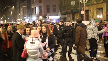 Karnevalisten stehen auf der Zülpicher Straße in der Nacht neben Polizisten.&nbsp;
