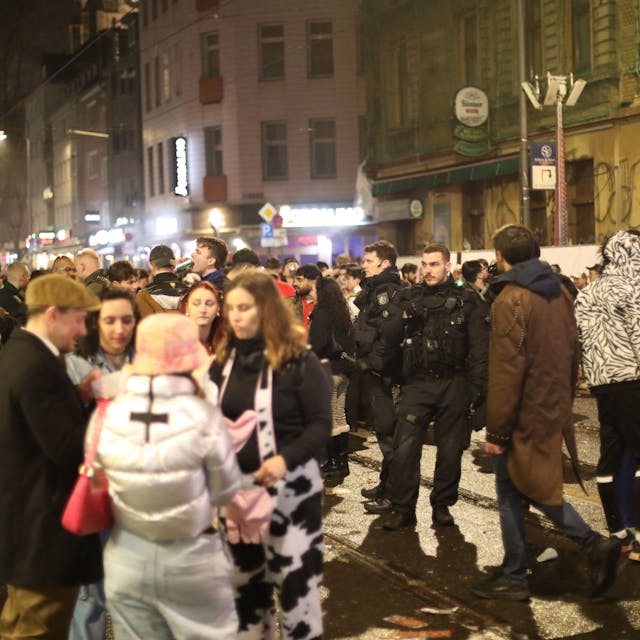 Karnevalisten stehen auf der Zülpicher Straße in der Nacht neben Polizisten.&nbsp;