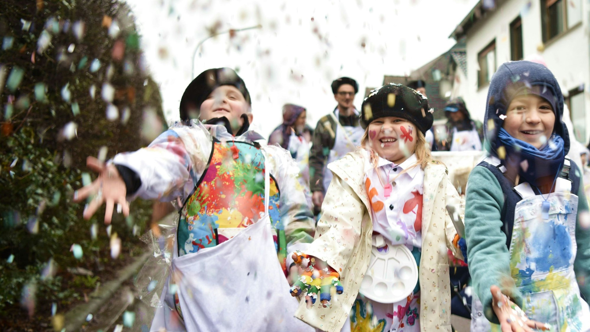 Drei zum Karneval verkleidete Kinder schmeißen beim Kinderzug in Kommern Konfetti.