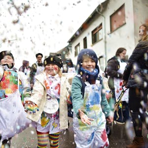Drei zum Karneval verkleidete Kinder schmeißen beim Kinderzug in Kommern Konfetti.