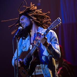 Der britische Schauspieler Kingsley Ben-Adir steht als Bob Marley Gitarre spielend und singend auf der Bühne. Er trägt eine Jeansjacke, seine Rastazöpfe&nbsp;