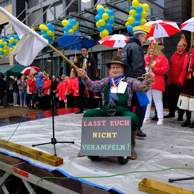 Bürgermeister Hans-Peter Schick sitzt auf einem Spielzeugtrecker und schwenkt die weiße Fahne. In der linken Hand hält er den Stadtschlüssel, den er an die Jecken abgibt.