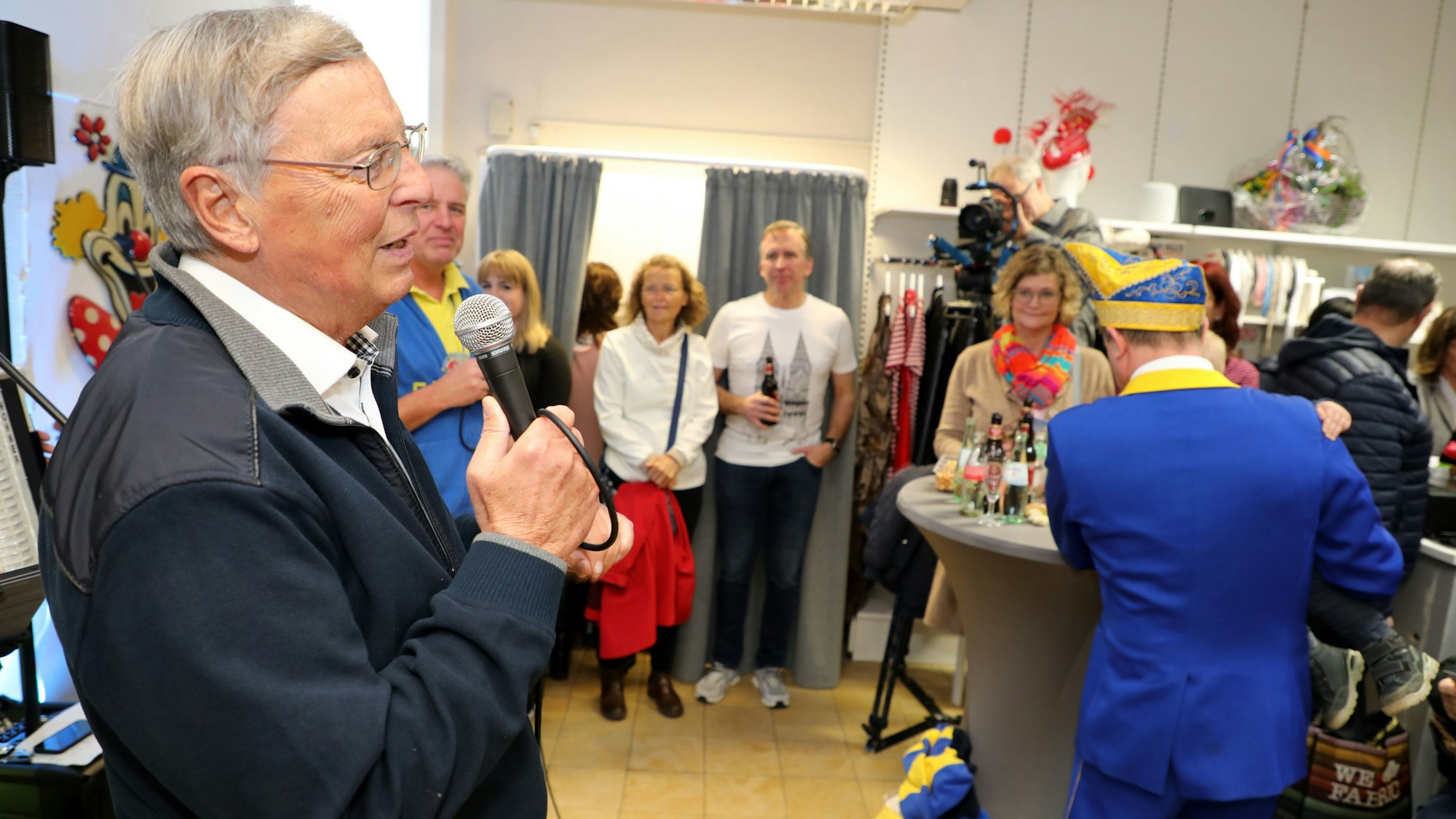 Politiker Wolfgang Bosbach  spricht mit einem Mikro zu den Eröffnungsgästen im Laden „Jeck jemaat“ in Bergisch Gladbach-Heidkamp.