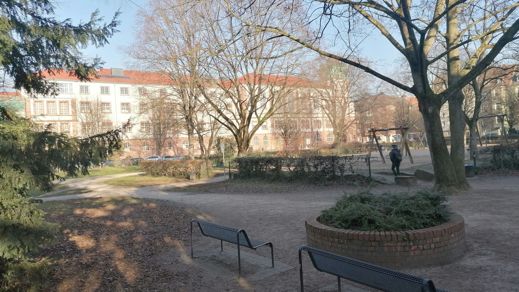 Zu sehen ist der Leipziger Platz, im Vordergrund Sitzbänke, im Hintergrund das Leonardo-da-Vinci-Gymnasium.